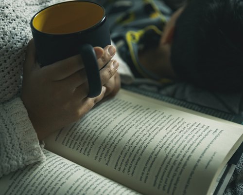 Person relaxing and reading a book with a warm cup of coffee